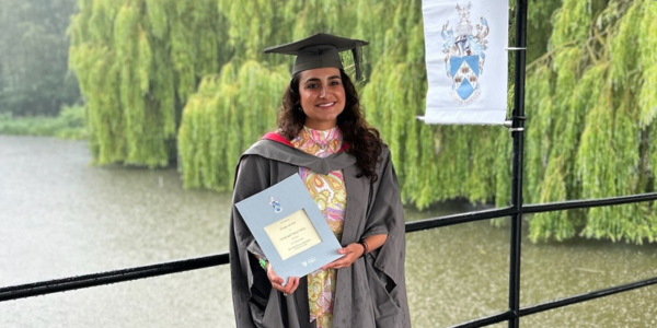 Ana Pau is at graduation holding her degree certificate on the Spring Lane bridge